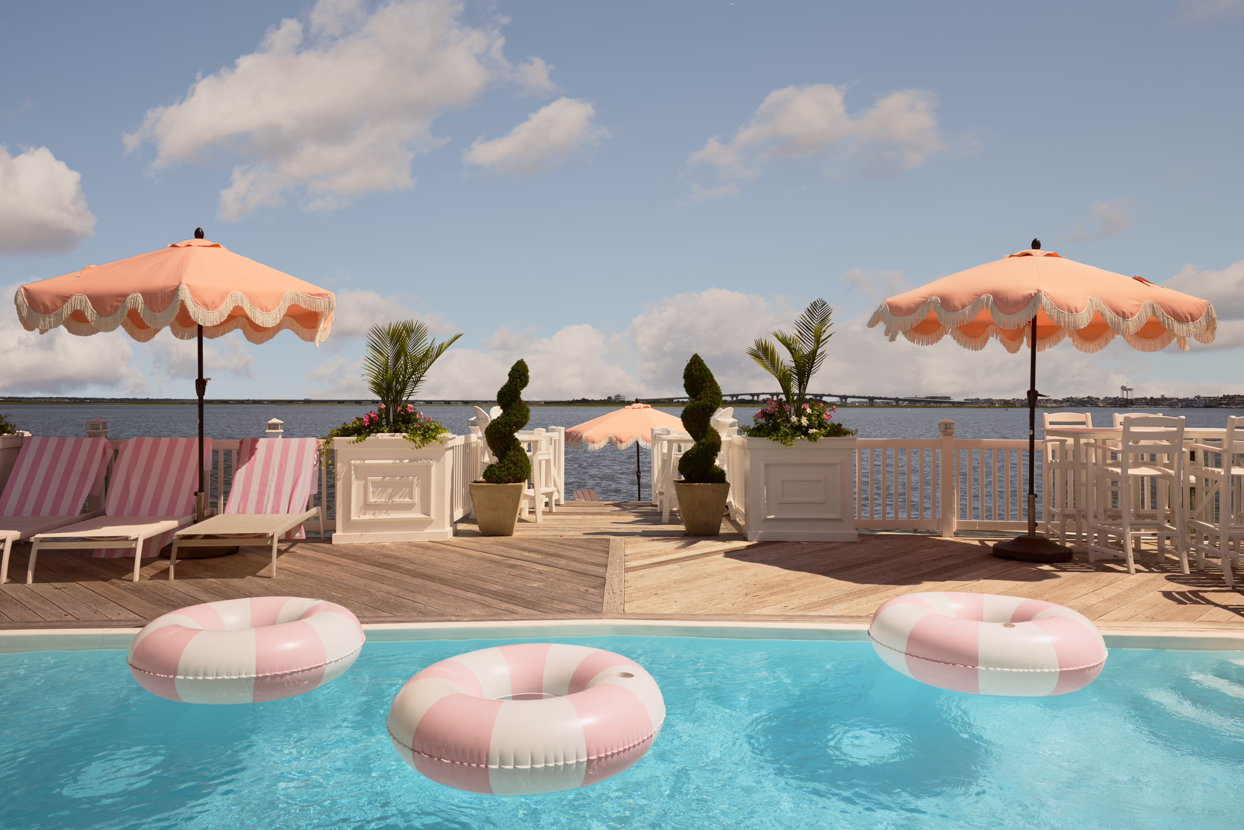 Bayshore pool deck with pink umbrellas, striped floats and a view across the bay