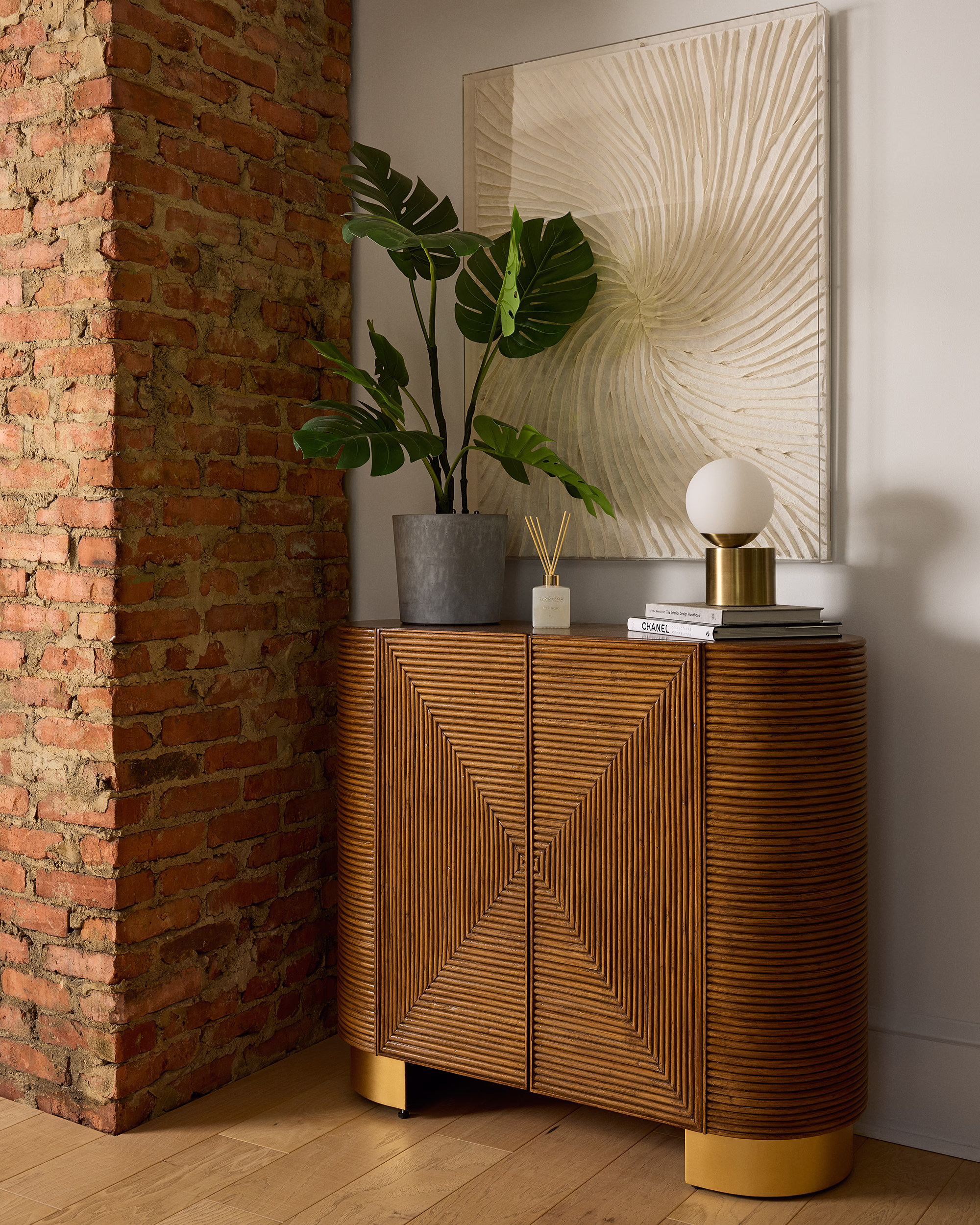 Sculptural wood cabinet beside an exposed brick wall and potted plant