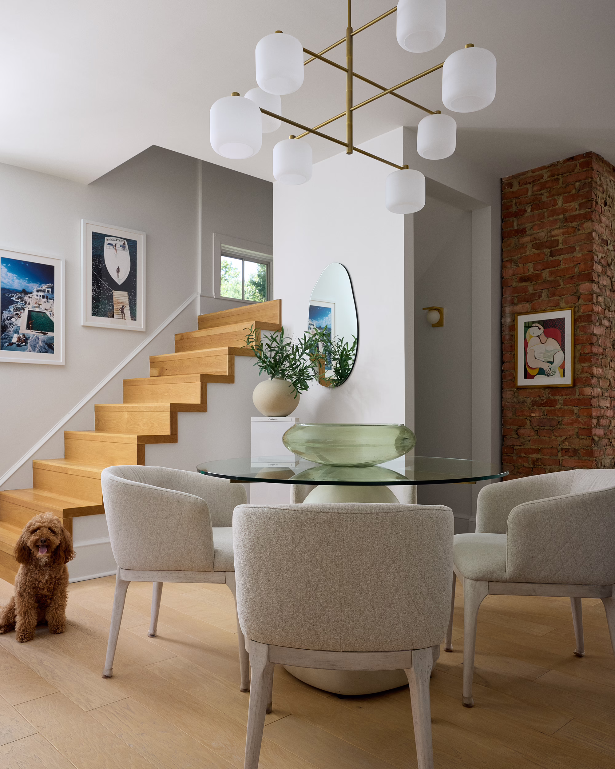 Station dining area with a glass table, open wood staircase, exposed brick and a small dog